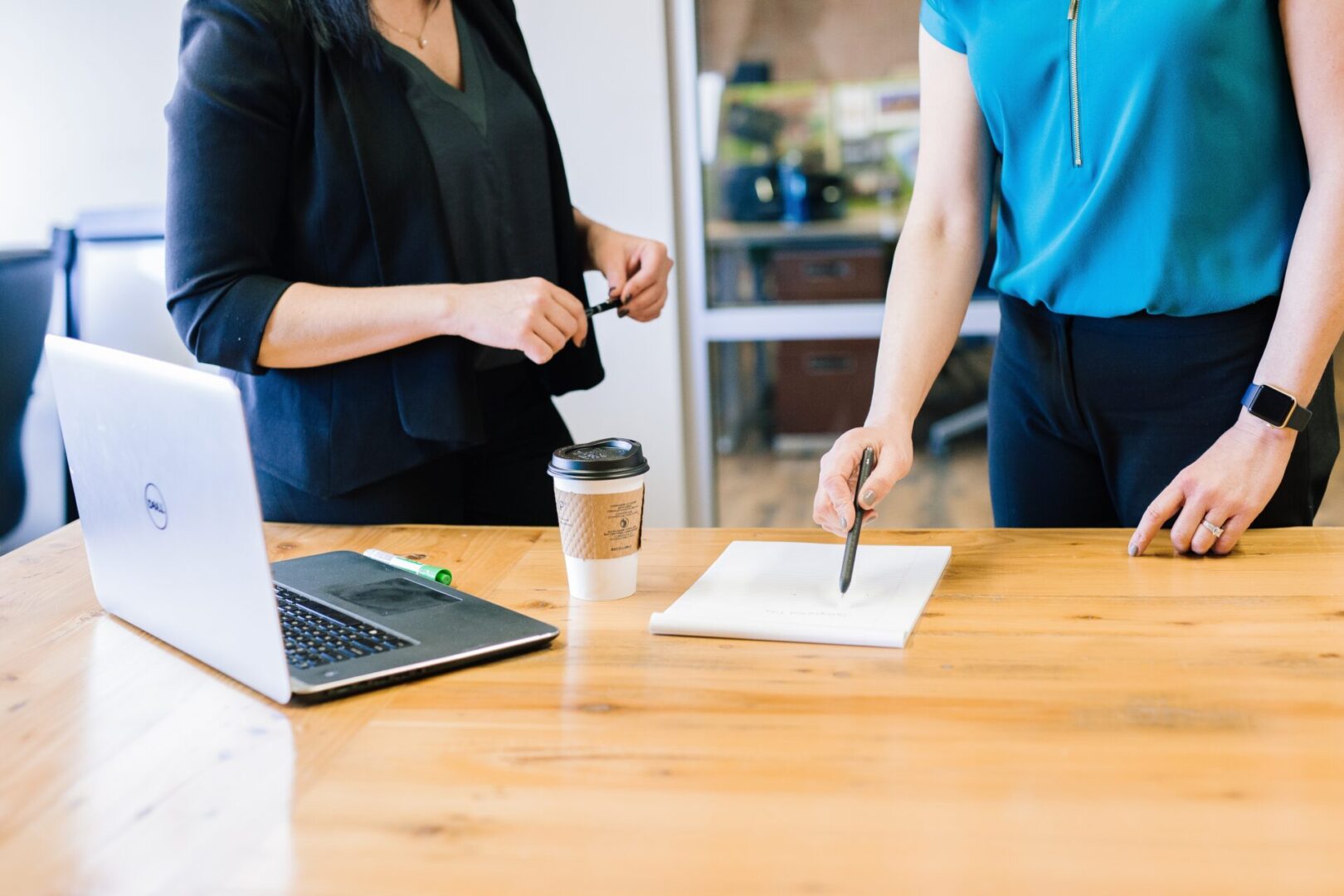 Two colleagues standing at a table with papers and coffee, discussing business details in a productive office environment