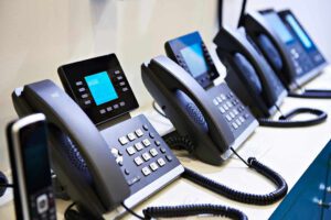 A row of black office phones with digital displays and coiled cords, part of our Office PBX telephone service, are lined up on a white surface.